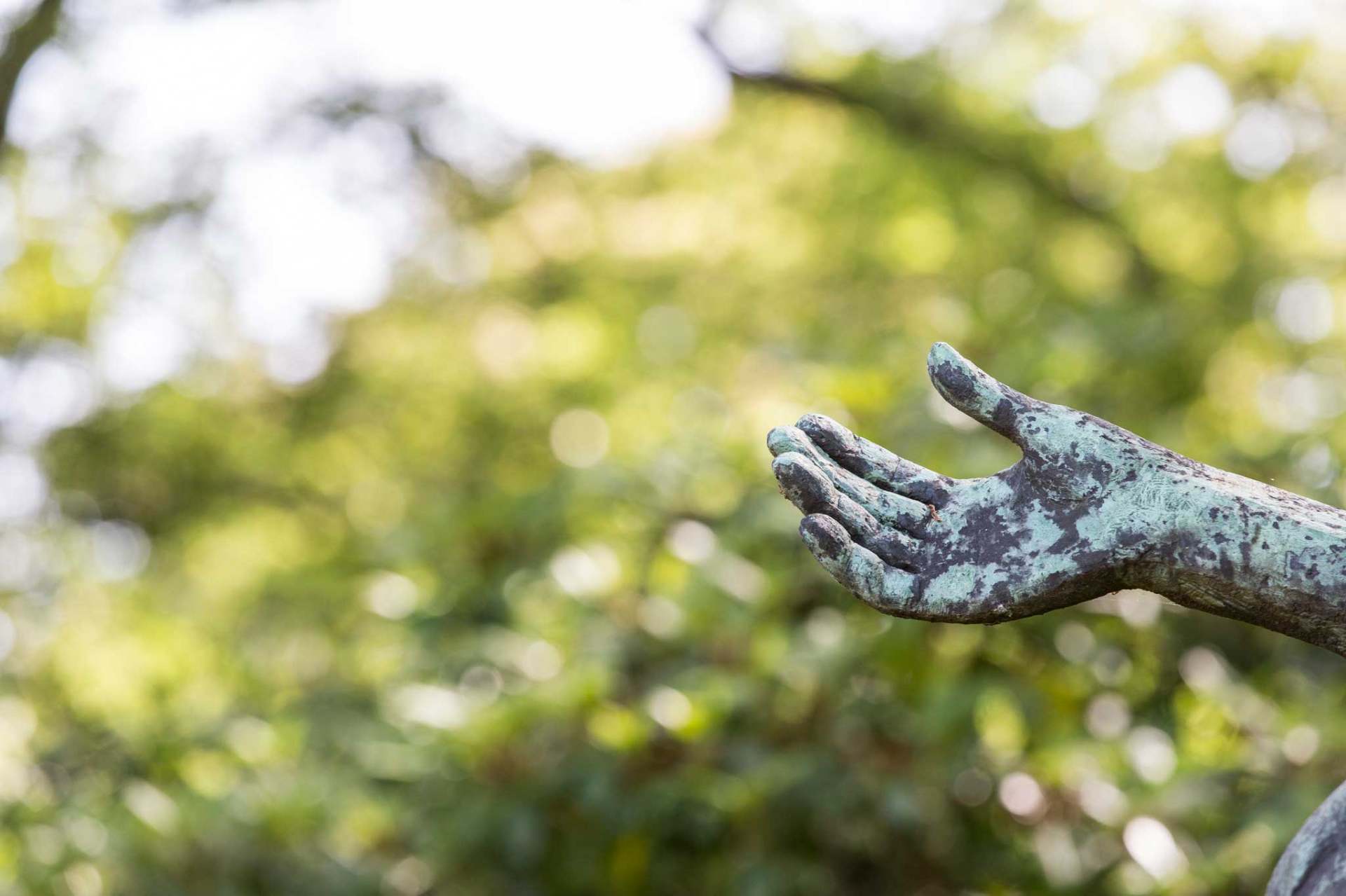 Bronzene offene Hand einer Skulptur vor grünem Blattwerk