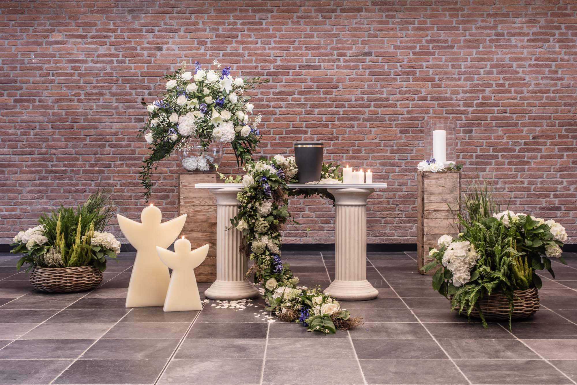 Urne auf Säule mit weißen Blüten und Engelsfiguren
